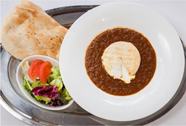 A dish of curry with naan bread and a small salad on the side, served on a silver tray.