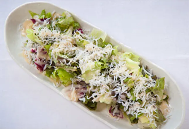 A long plate of fresh salad topped with small white fish (shirasu), placed on a white tablecloth.