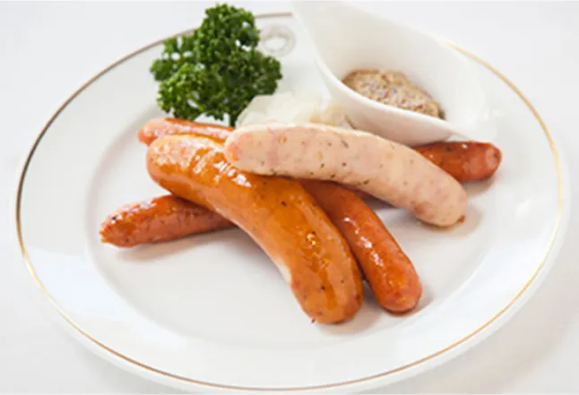 A plate of assorted sausages with mustard and garnished with parsley, served on a white dish.