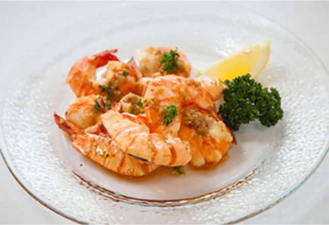 A seafood dish featuring cooked shrimp, garnished with lemon and parsley, served on a glass plate.