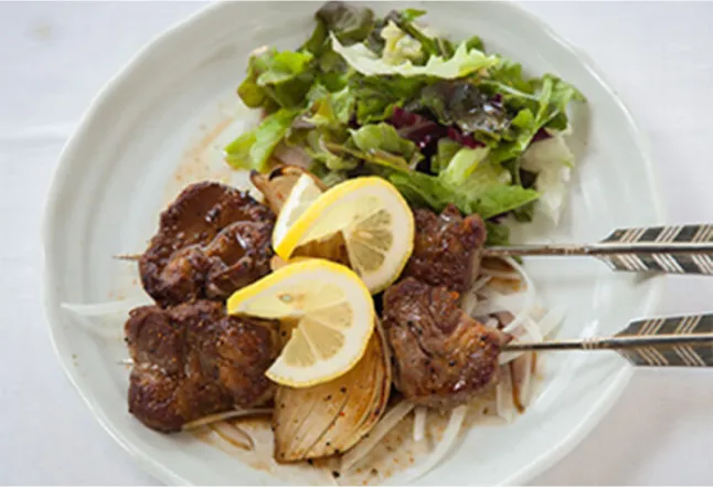 A plate of grilled meat skewers with lemon wedges, served with a side salad.