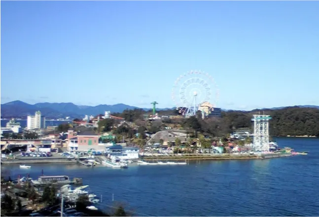 A scenic view of a lakeside amusement park with a ferris wheel and various attractions, under a clear blue sky.