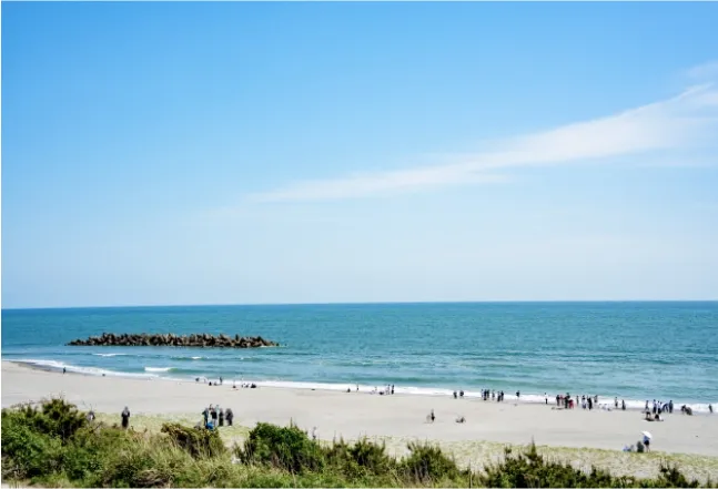 A calm beach scene with people walking along the shore and a blue ocean stretching out to the horizon.